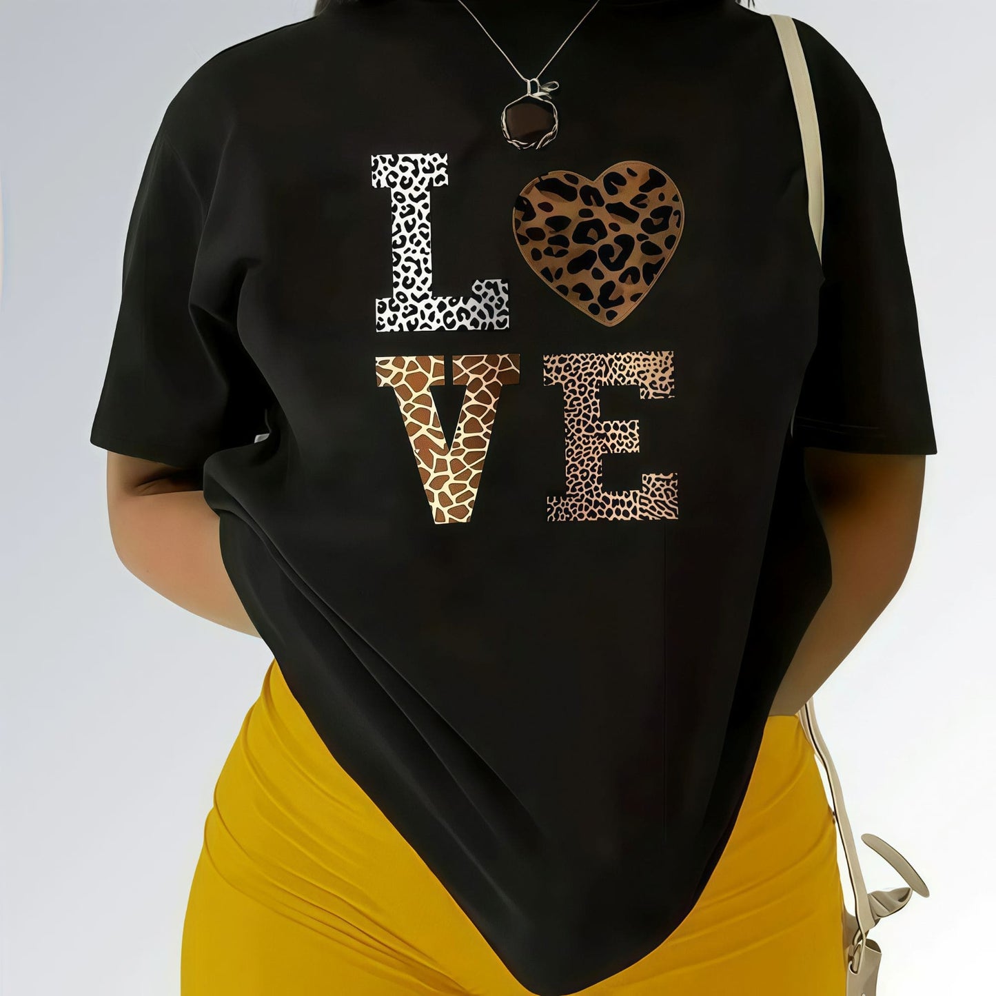 Modelo vestida com uma camisa preta feminina com estampa LOVE em animal print e shorts cor mostarda.