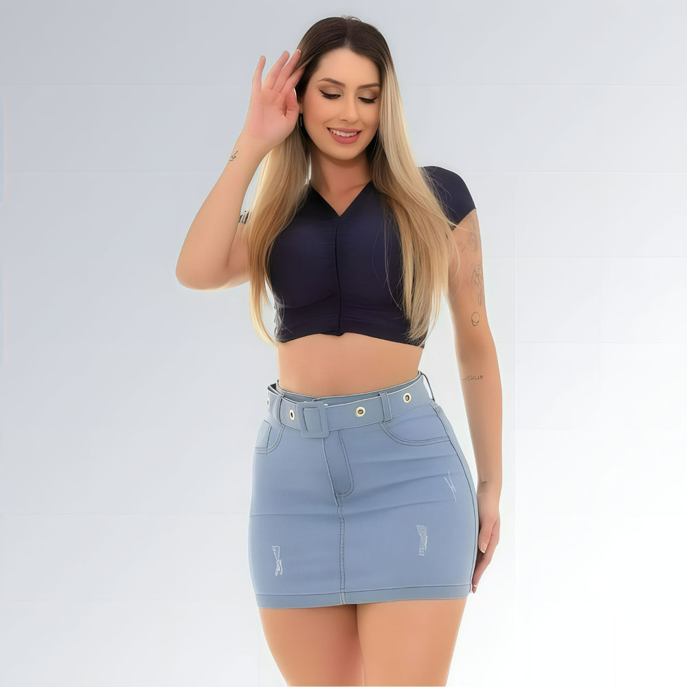 Mini saia jeans feminina azul clara com cintura alta, cinto com ilhós metálicos, bolsos frontais e leve desgaste na barra.