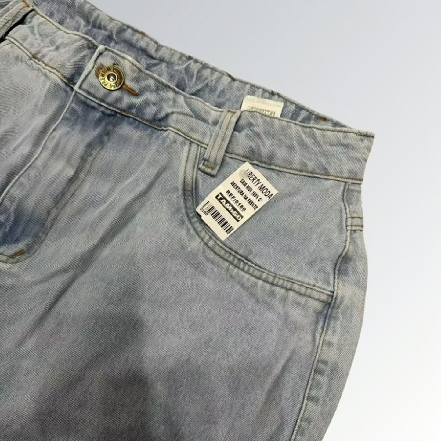 Saia jeans denim essential feminina azul clara com design clássico de cinco bolsos, fenda frontal e detalhe de costura central — peça versátil disponível para venda online de moda casual.