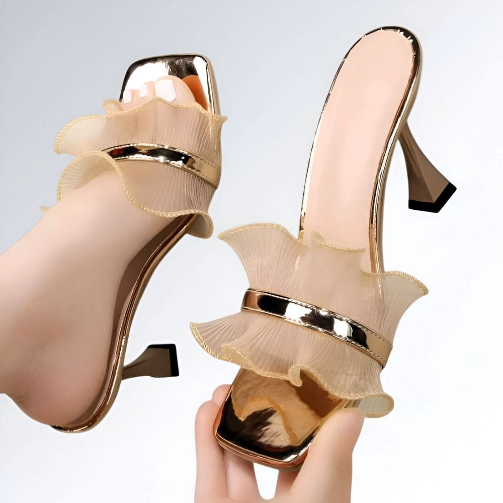 Tamanco feminino dourado com salto alto, tiras plissadas transparentes e detalhe metálico central.