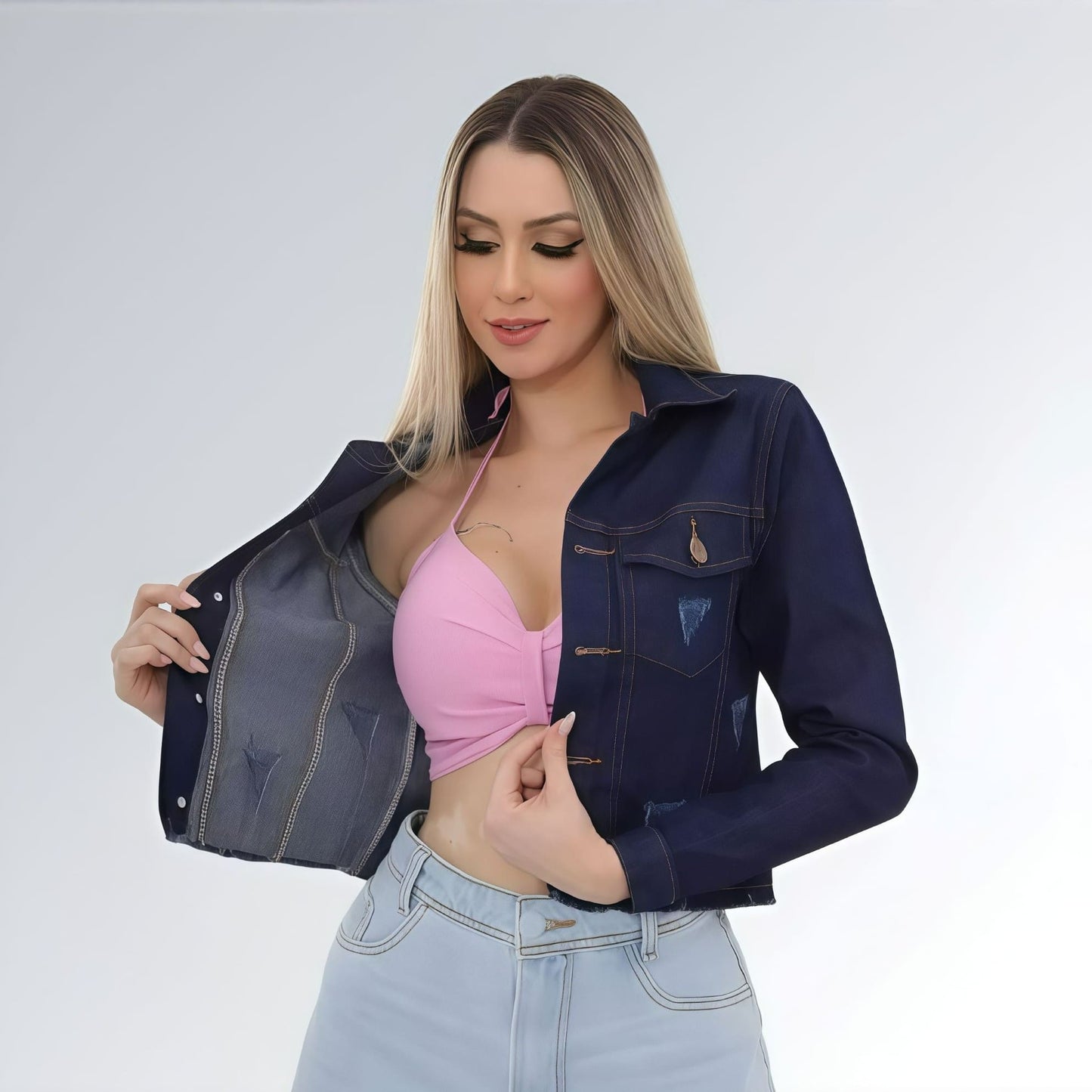 Jaqueta jeans cropped feminina azul escuro com puídos, bolsos frontais com aba e fechamento por botões.