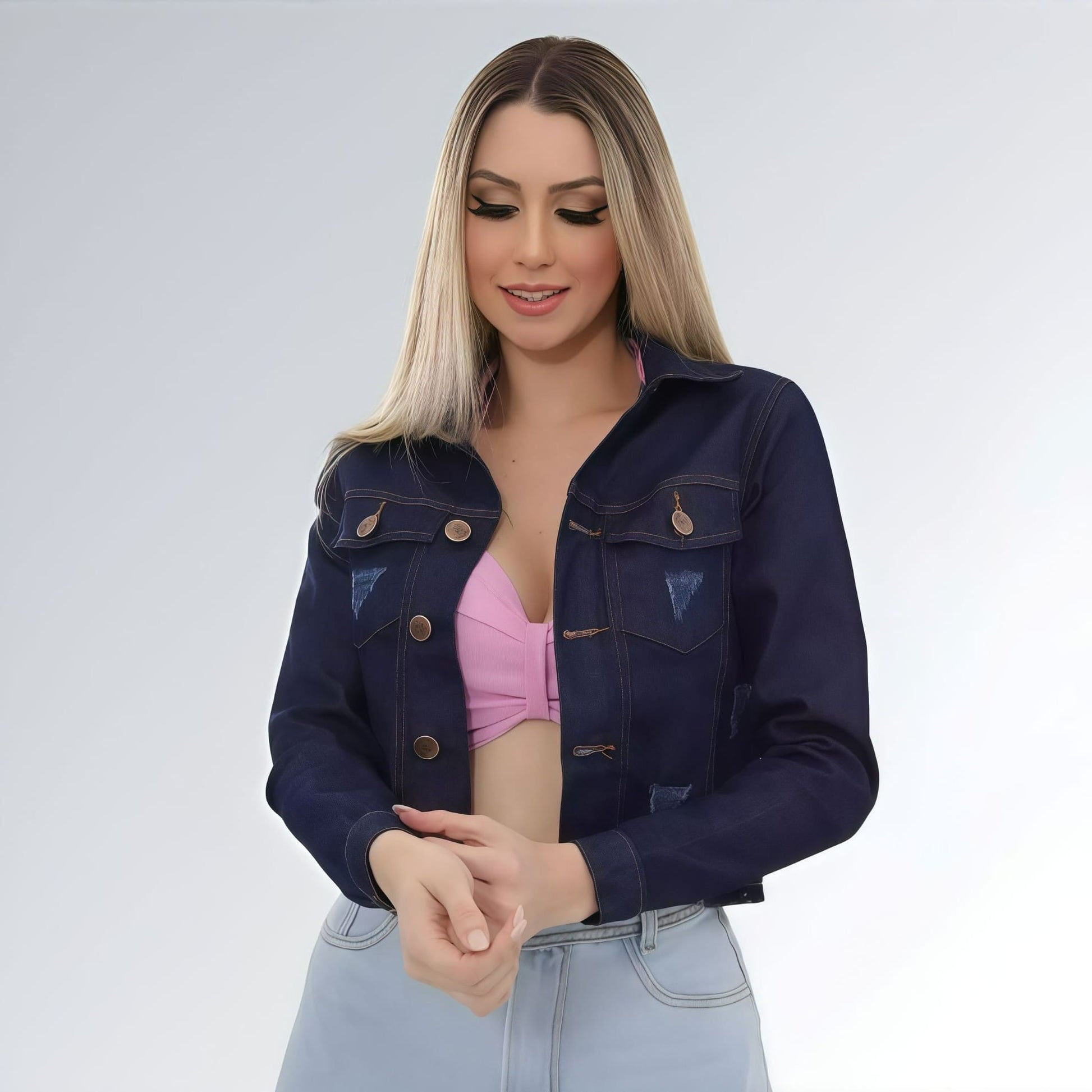 Jaqueta jeans cropped feminina azul escuro com puídos, bolsos frontais com aba e fechamento por botões.