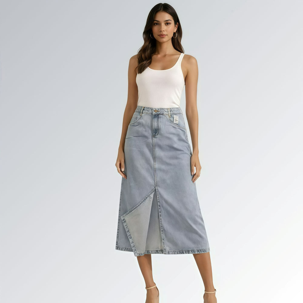 Saia jeans denim essential feminina azul clara com design clássico de cinco bolsos, fenda frontal e detalhe de costura central — peça versátil disponível para venda online de moda casual.