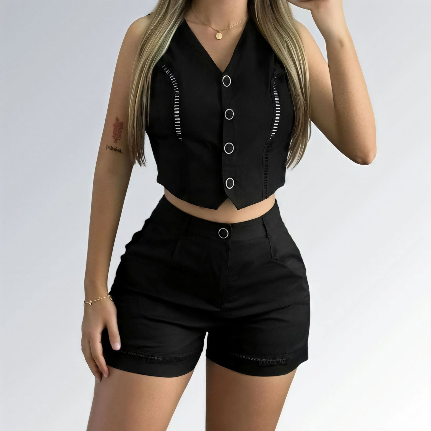 Conjunto feminino preto com top cropped sem mangas, decote V com botões prateados e short de cintura alta com detalhe metálico.