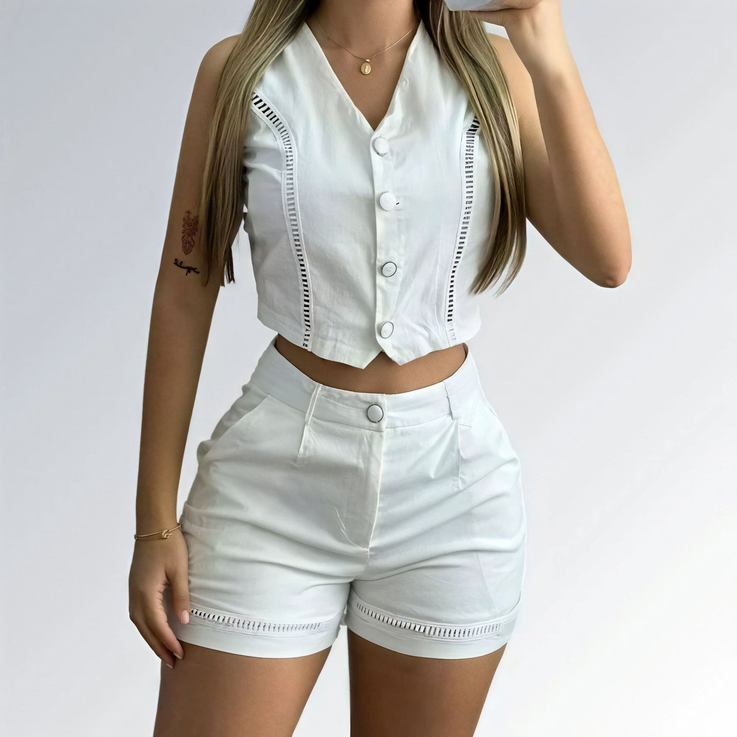 Conjunto feminino branco com top cropped sem mangas, decote V com botões prateados e short de cintura alta com detalhe metálico.