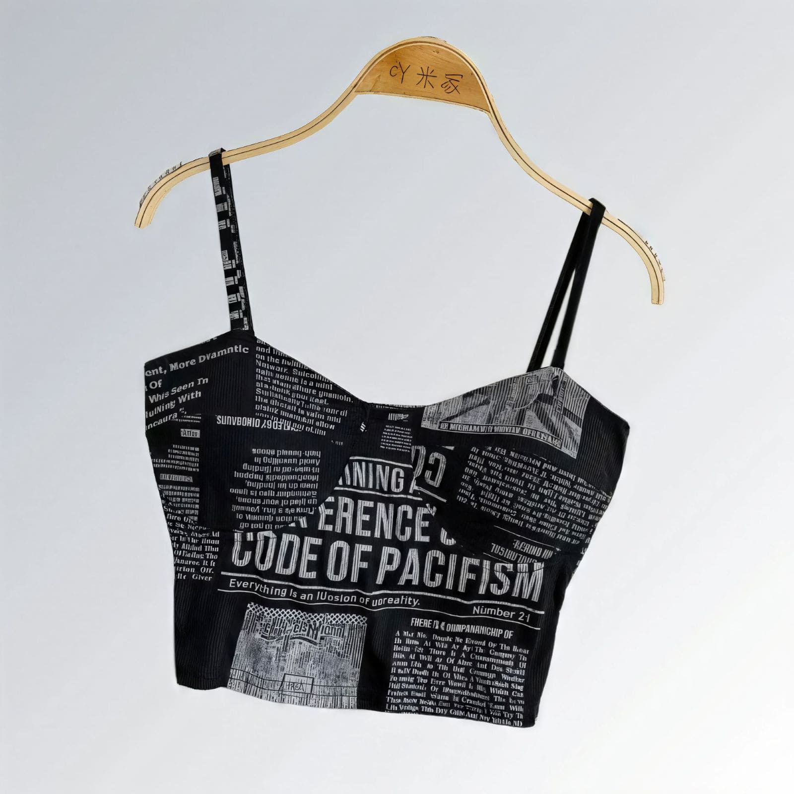 Top suspensório feminino cropped com bojo, estampa jornal preto e cinza, alças largas e estilo urbano.